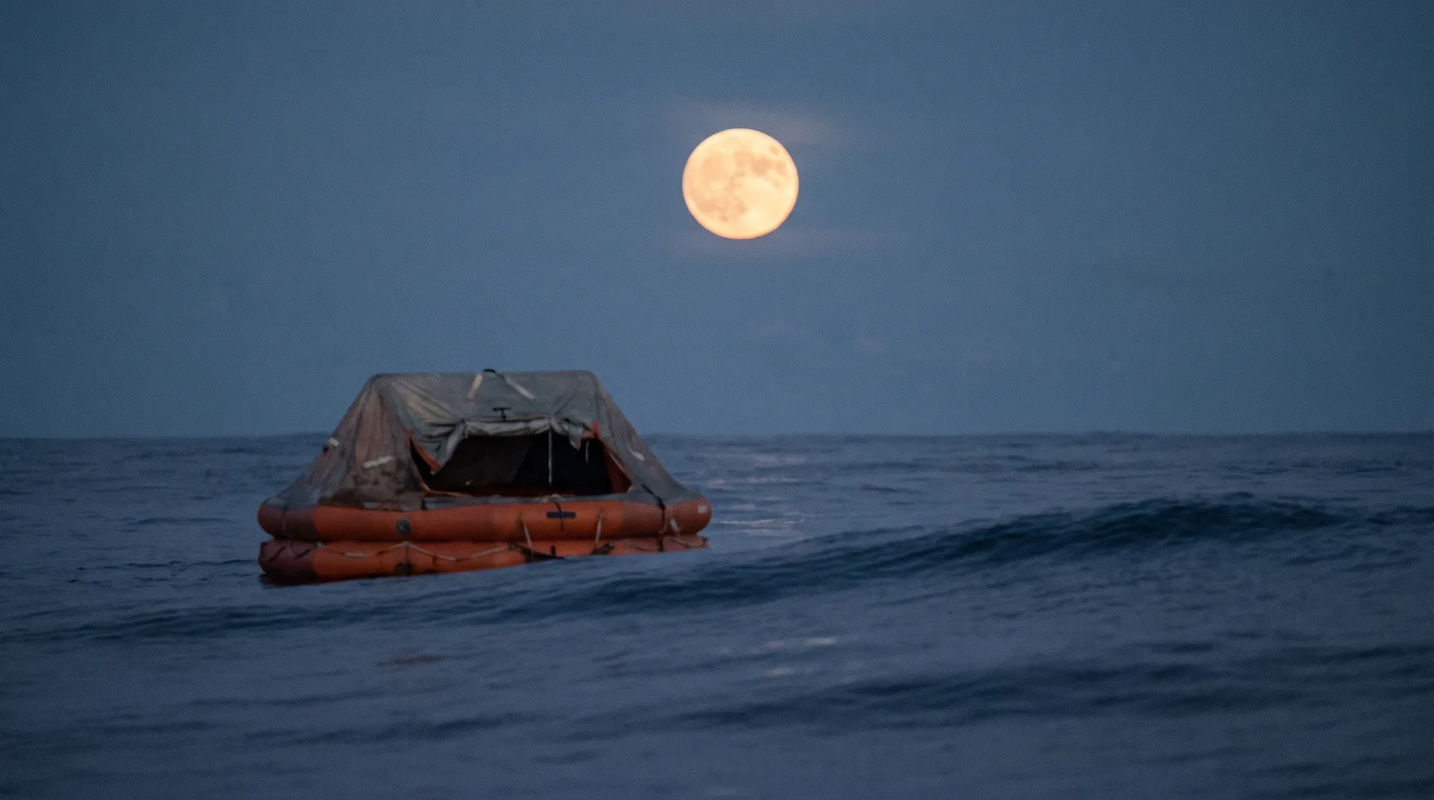 Balsa salvavidas naranja con toldo a la deriva sobre mar de fondo con luna llena