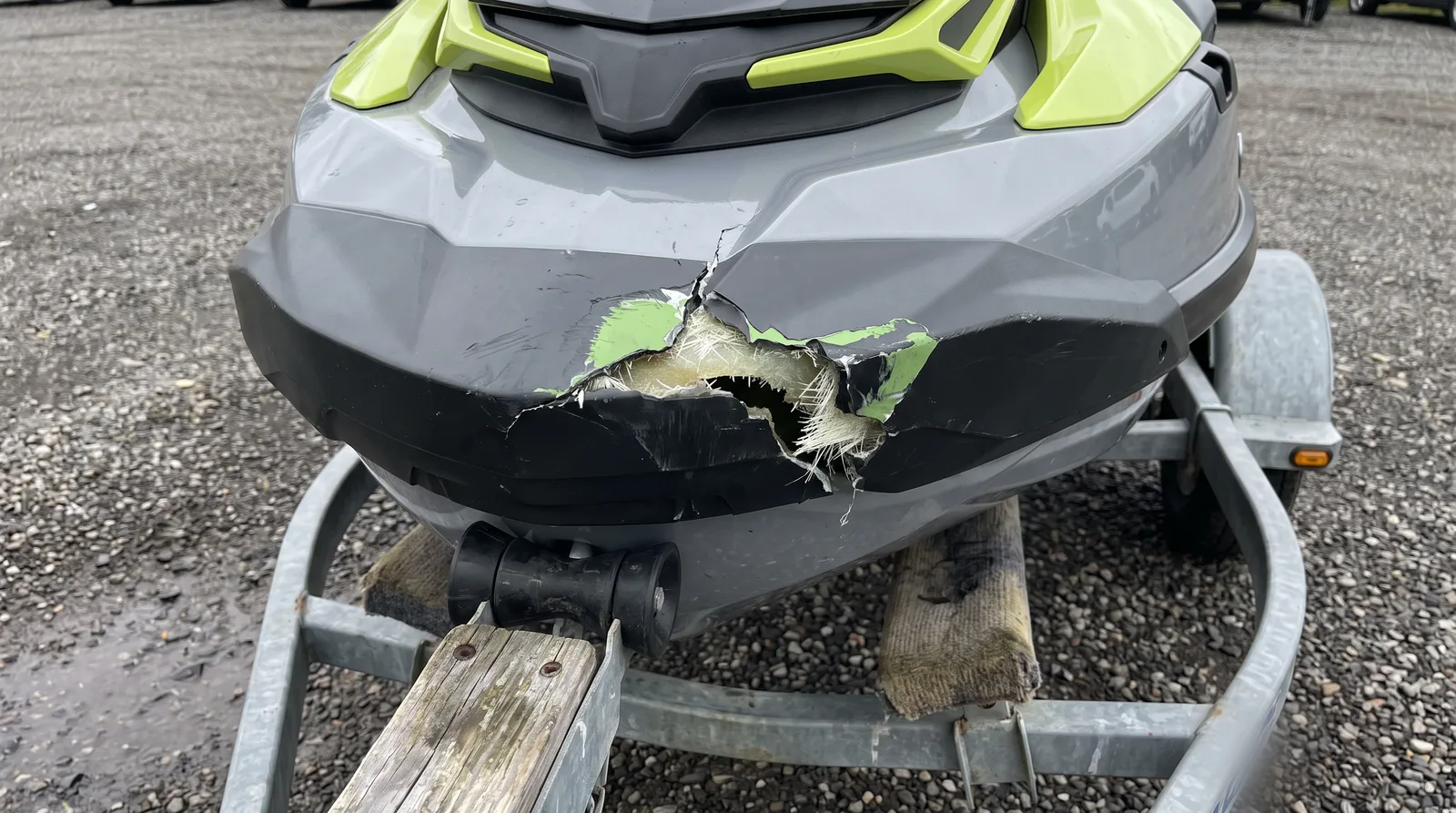 Proa de una moto de agua blanca sobre su remolque, con una grieta y el gelcoat desconchado tras un golpe.