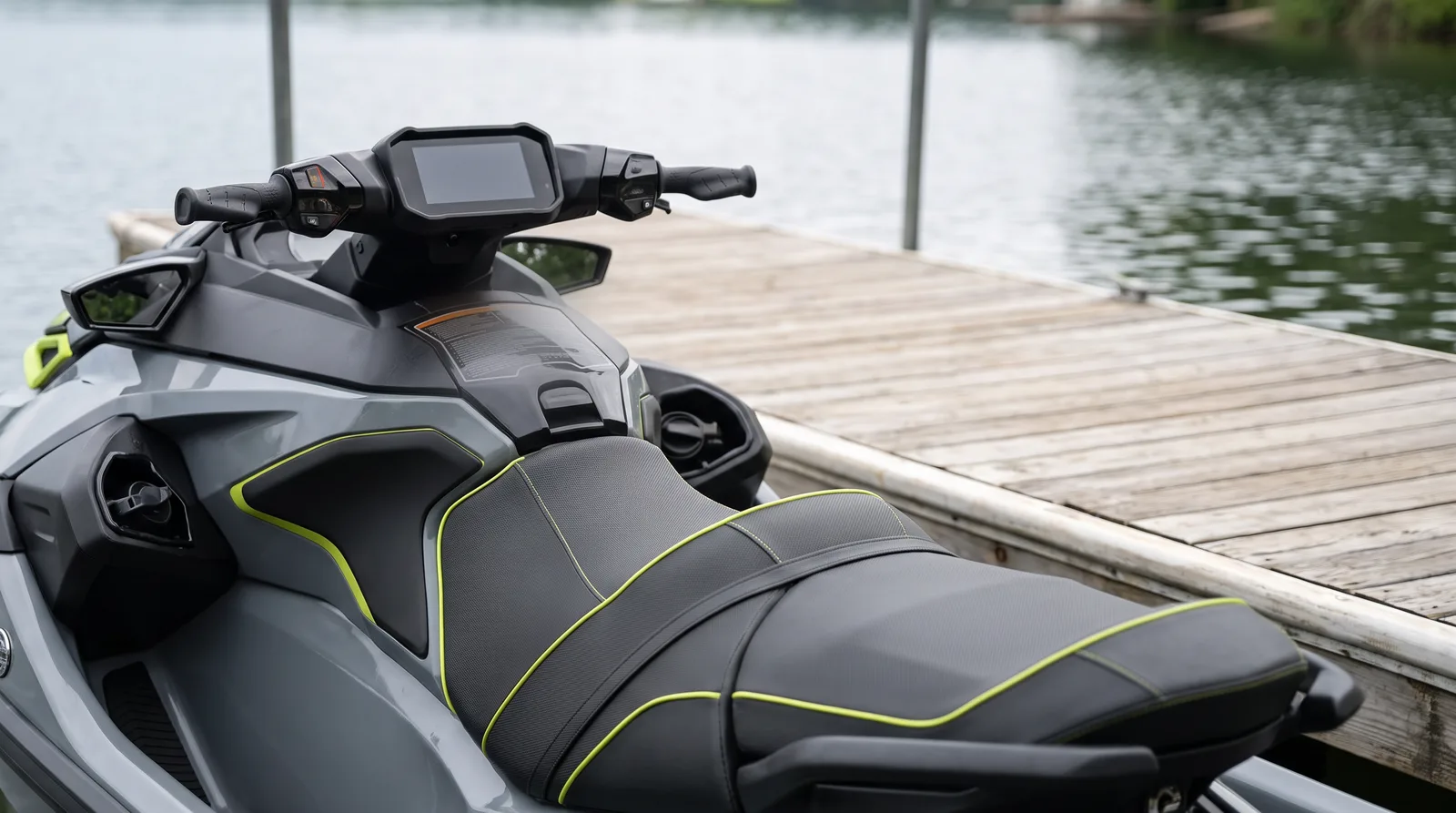 Manillar y largo asiento gris de una moto de agua moderna junto a un pantalán de madera, con el lago desenfocado al fondo.