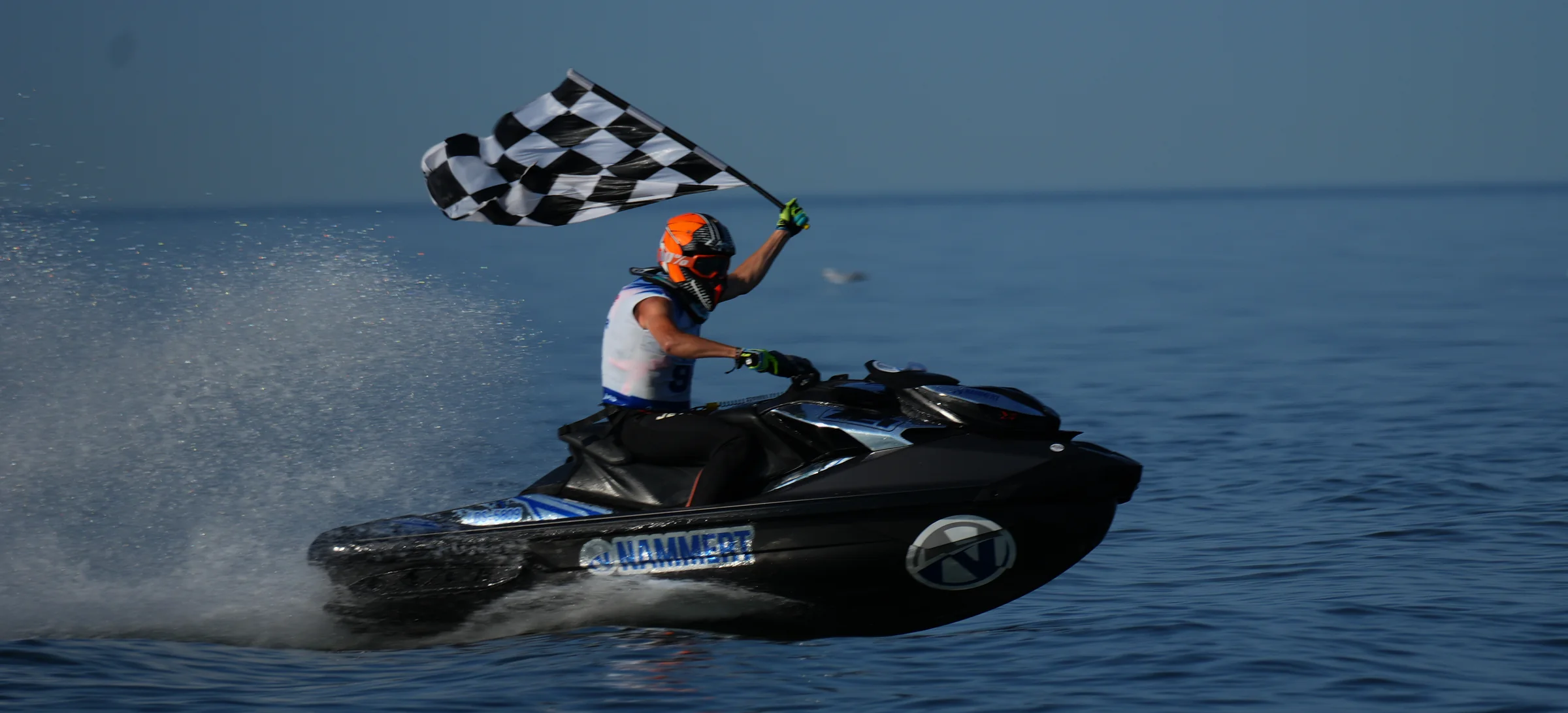 Piloto de moto de agua con el logo de NAMMERT y dorsal ondeando la bandera a cuadros en la meta
