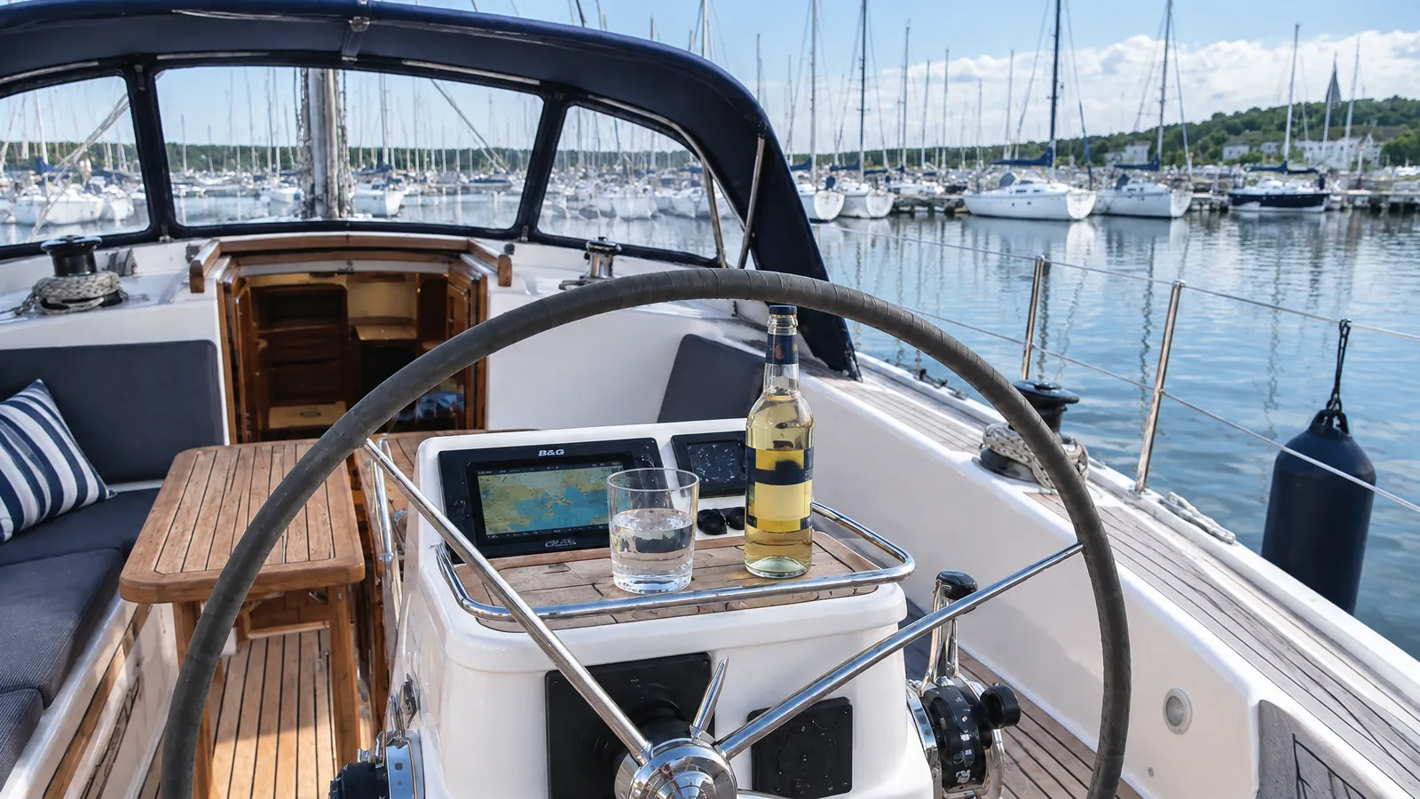 La bañera de un velero a pleno sol, un vaso de agua y una bebida sin alcohol junto al timón