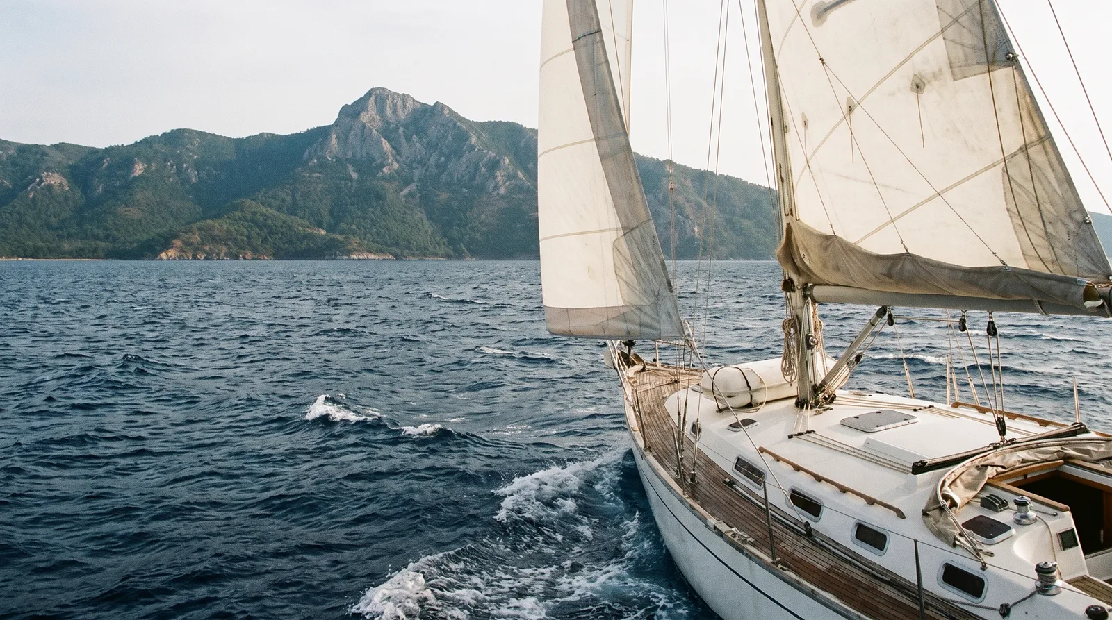 Velero navegando frente a una península boscosa con un pico rocoso alto en el norte del Egeo