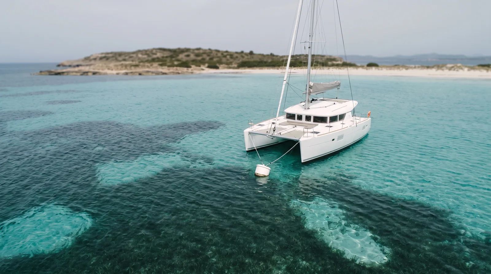 Catamarán de vela en una boya sobre arena clara junto a una pradera de posidonia