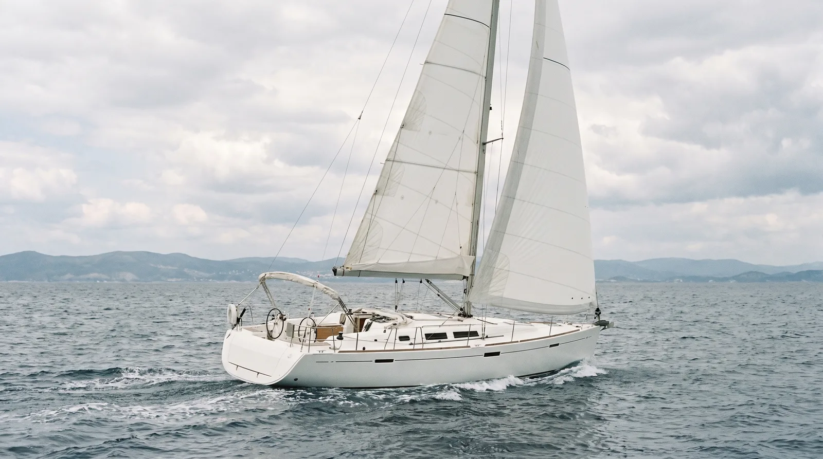 Velero de chárter blanco navegando a toda vela en mar abierto con una costa lejana al fondo