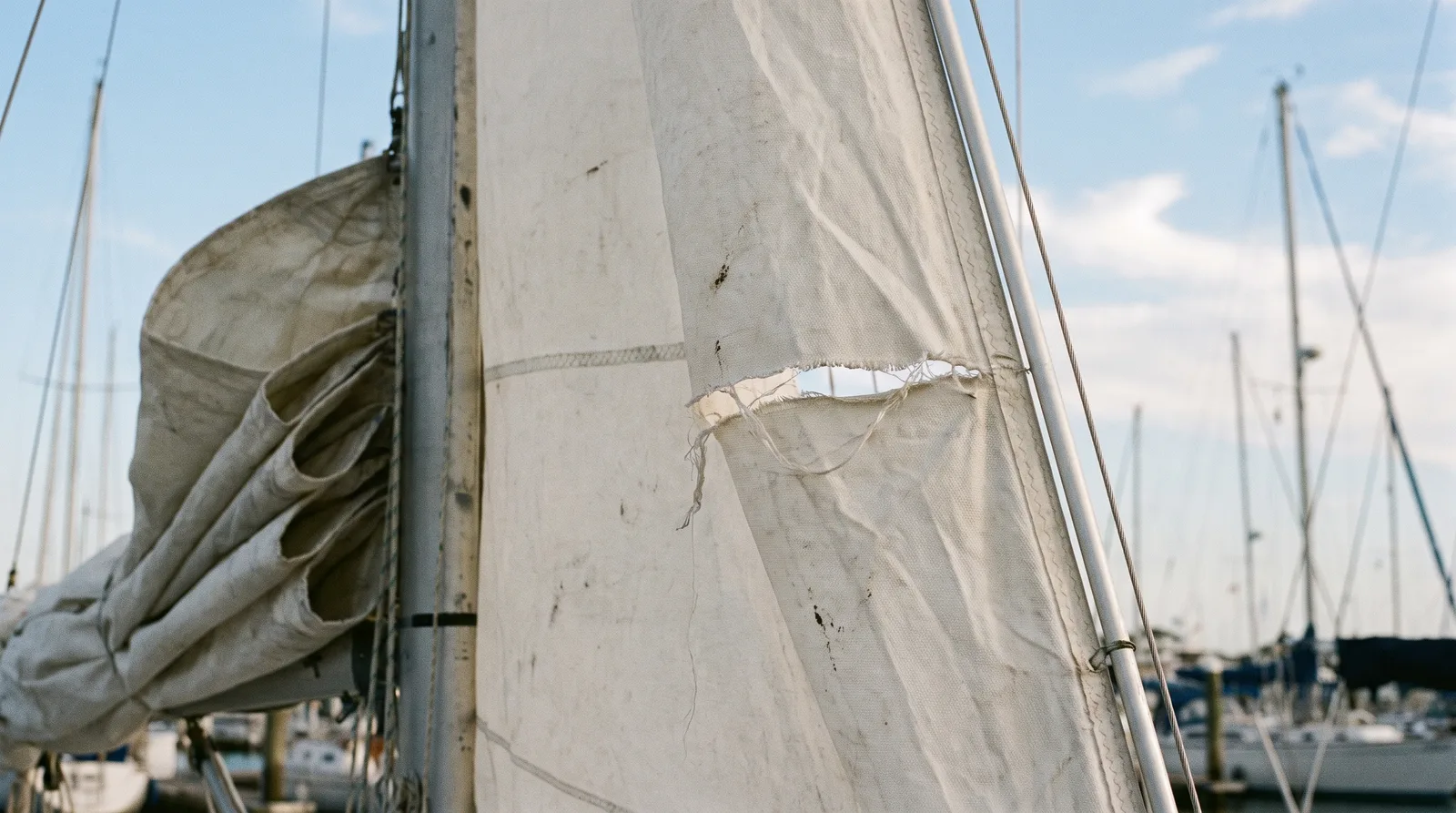 Vela de proa blanca de un barco de chárter con un desgarro claro cerca de la baluma, contra un cielo azul