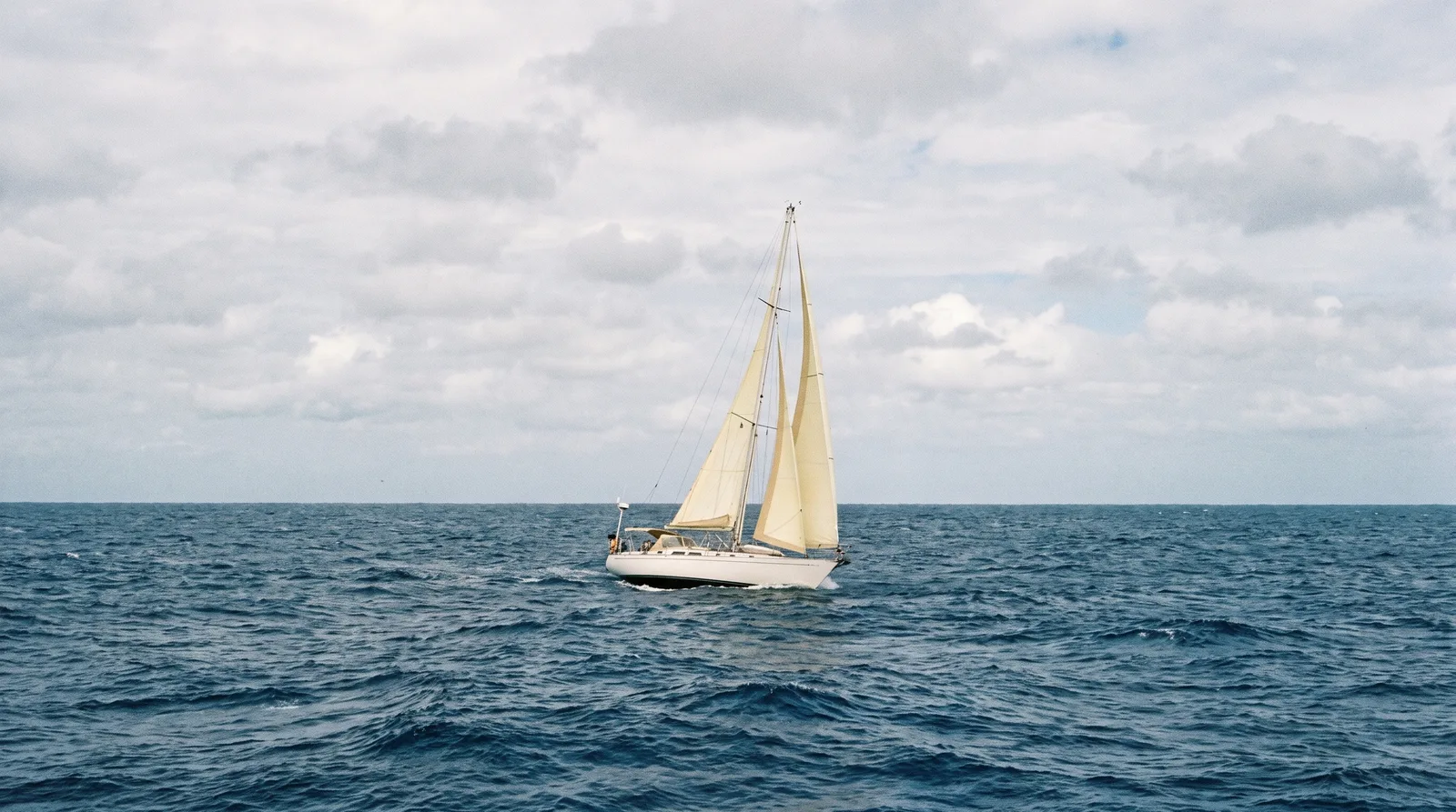 Un velero navega solo en mar abierto, sin costa a la vista en el horizonte