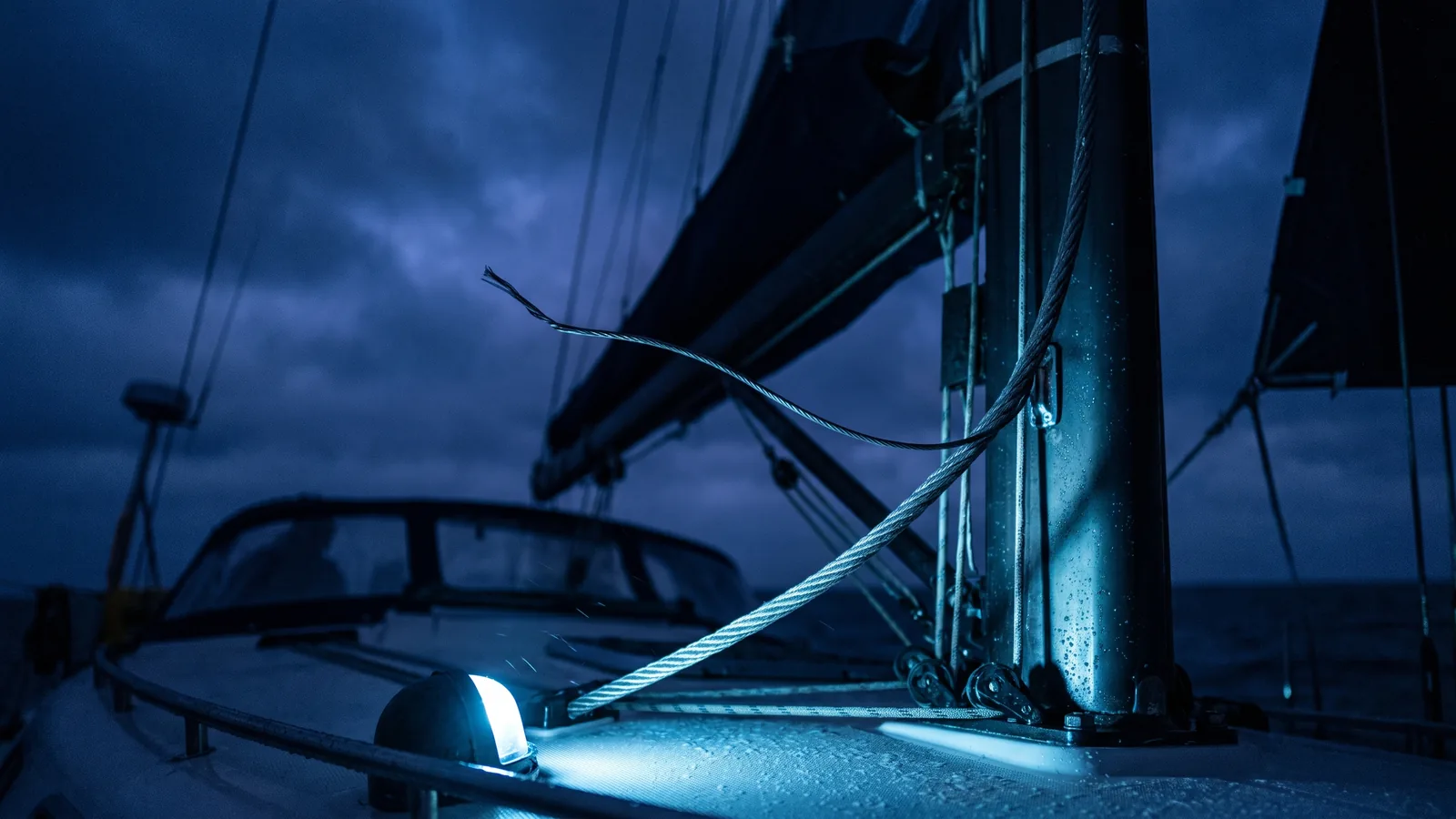 Primer plano del palo y la jarcia firme de un velero de noche, con una hebra del cable levantada