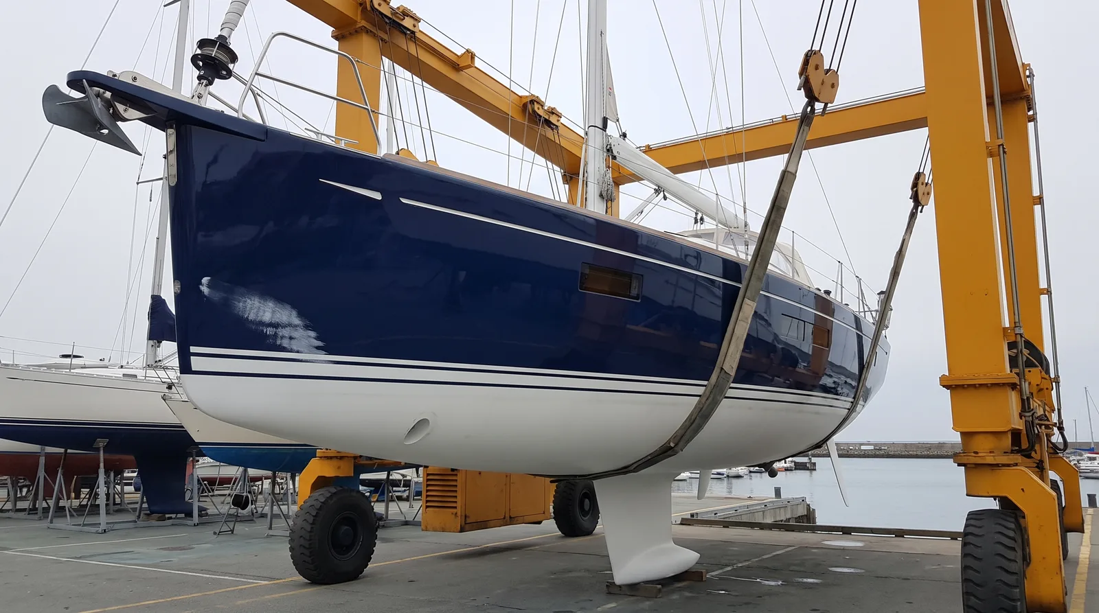 Velero azul bien cuidado colgado del travelift de un varadero para sacarlo a tierra y repararlo